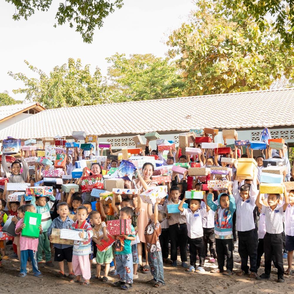 A large group photo of children and students holding up their gift boxes, celebrating the success of the Holiday Box Project.