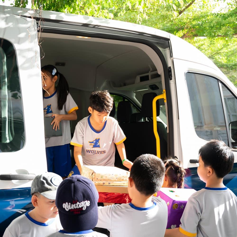 Children unloading gift boxes from a school van, preparing to deliver them to their recipients.