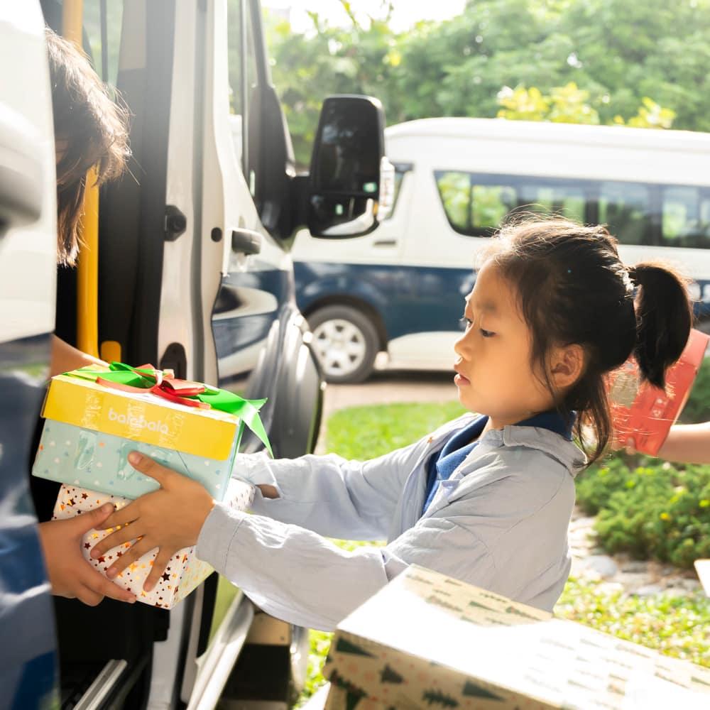 A child handing a decorated gift box to someone outside the school van during the Holiday Box Project.