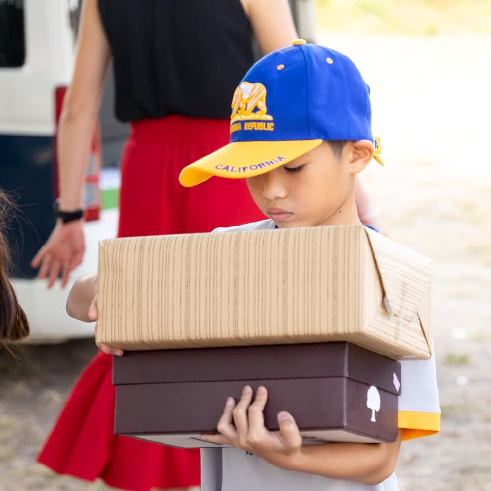 A student wearing a blue and yellow cap carrying multiple wrapped gift boxes to contribute to the project.