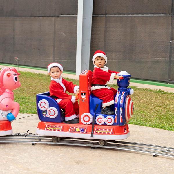 Young children dressed as Santa Claus enjoy a fun train ride decorated in bright holiday colors during the school Christmas event.