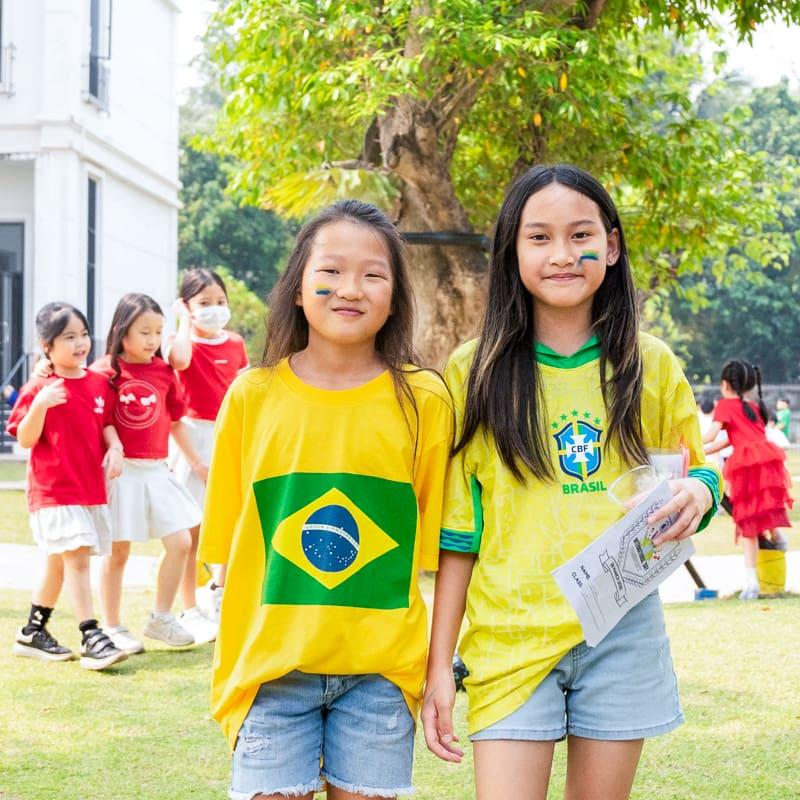 Two girls wearing Brazil football jerseys with painted cheeks, standing outside during International Day.
