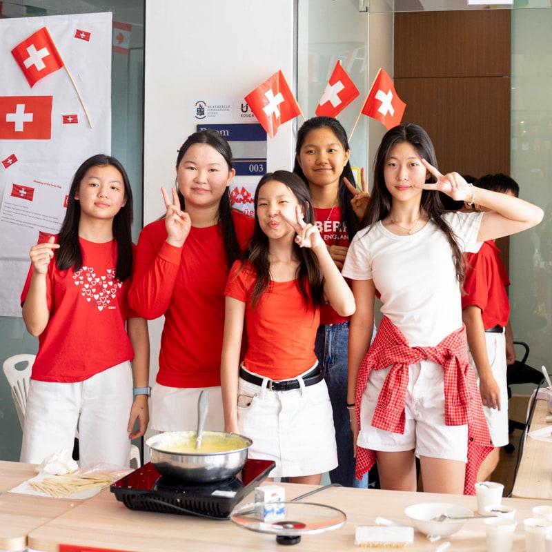 A group of older students dressed in red and white near a Swiss-themed booth.