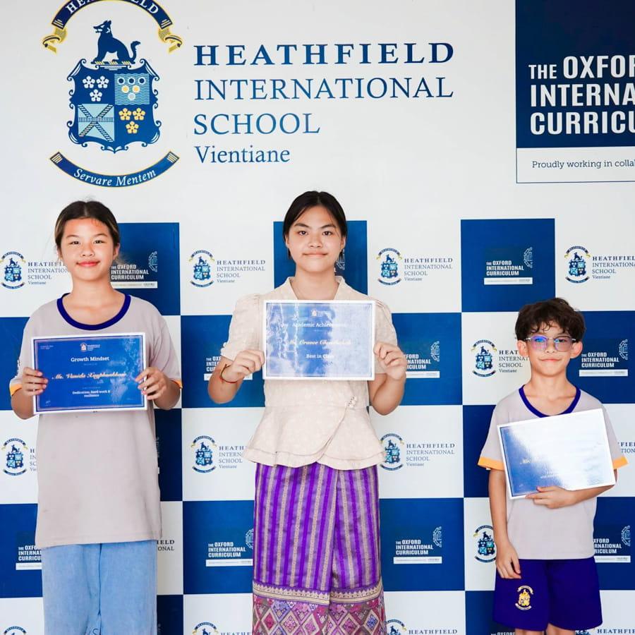 Three students smiling and holding achievement certificates