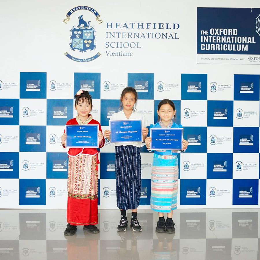 Three students smiling and holding achievement certificates