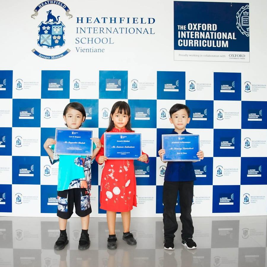 Three students smiling and holding achievement certificates