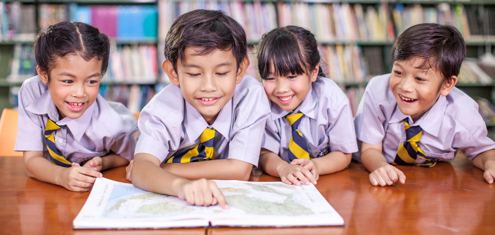 Engaged young learners exploring a map together in a school library.