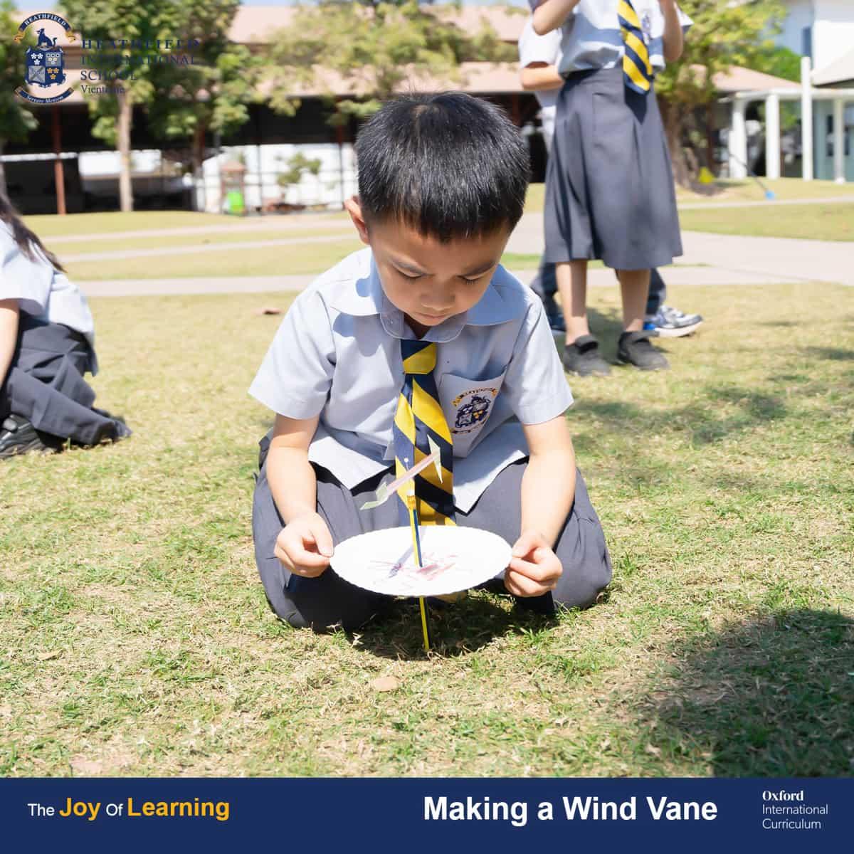 A student seated on the grass, carefully observing the completed wind vane to understand wind direction.